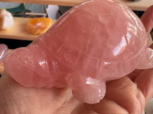 A polished pink quartz turtle sculpture held in a hand.